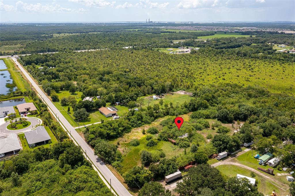 An aerial view shows a vacant, wooded lot marked with a red pin near a road — 10800 BILL TUCKER ROAD, WIMAUMA, FL