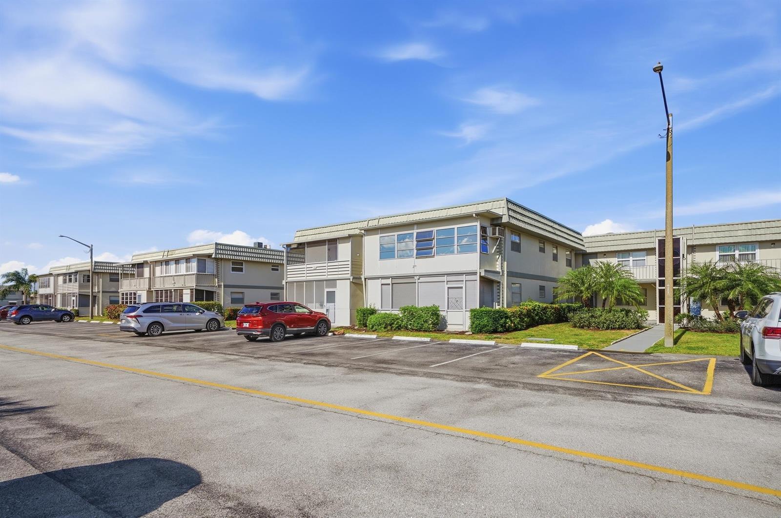 A multi-story apartment building with a parking lot in the foreground under a blue sky — 251 Monaco Way, Delray Beach FL 33446, DELRAY BEACH, FL