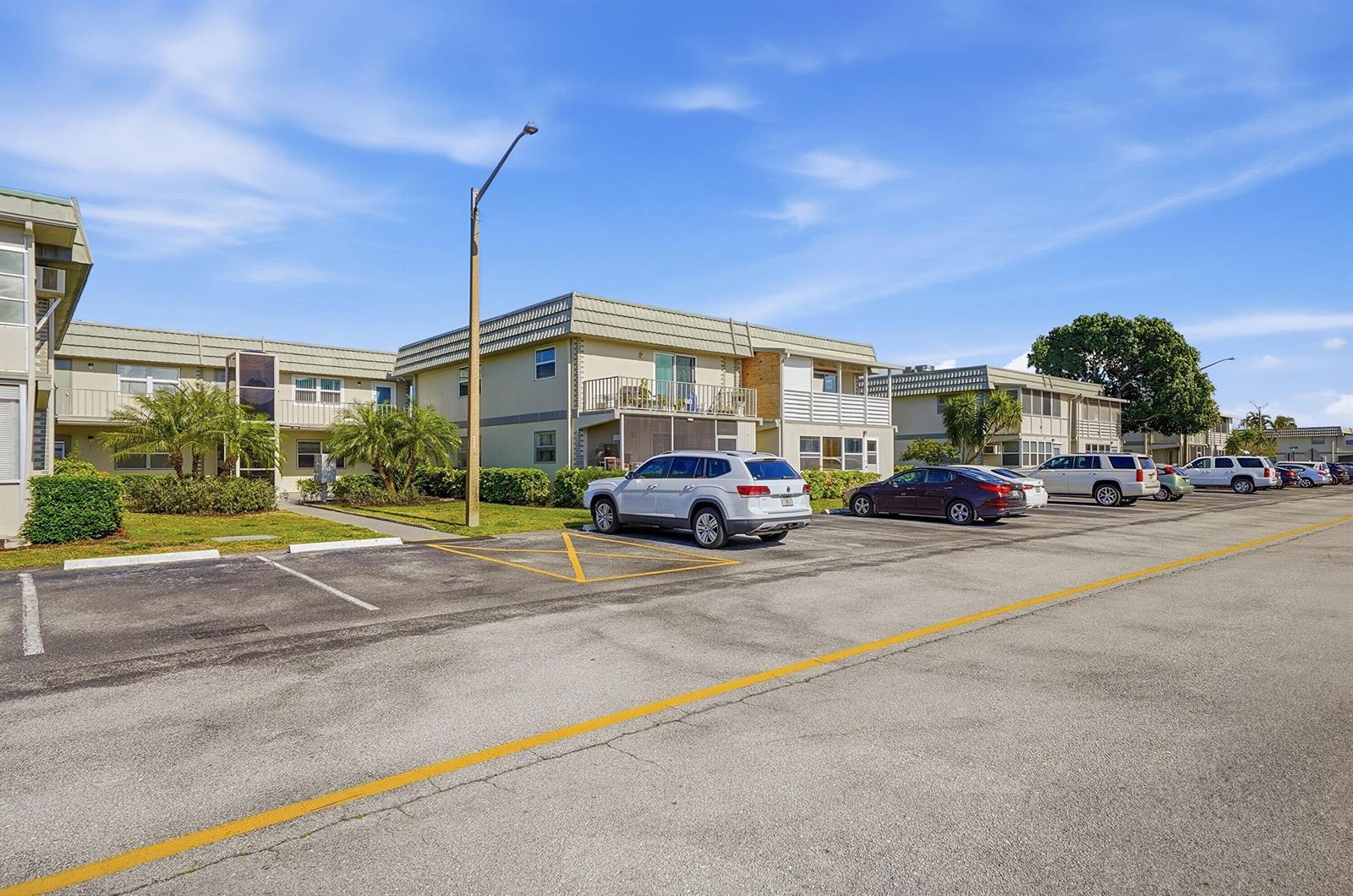 A parking lot sits in front of multi-story apartment buildings under a clear blue sky — 251 Monaco Way, Delray Beach FL 33446, DELRAY BEACH, FL