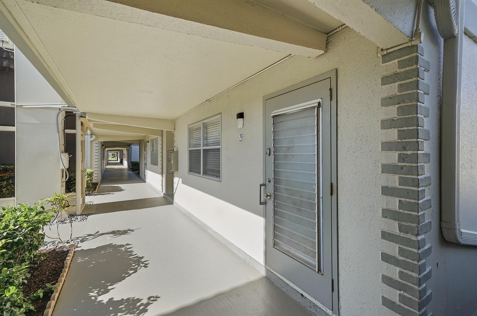 An exterior view of a covered apartment walkway featuring a grey door and window — 251 Monaco Way, Delray Beach FL 33446, DELRAY BEACH, FL