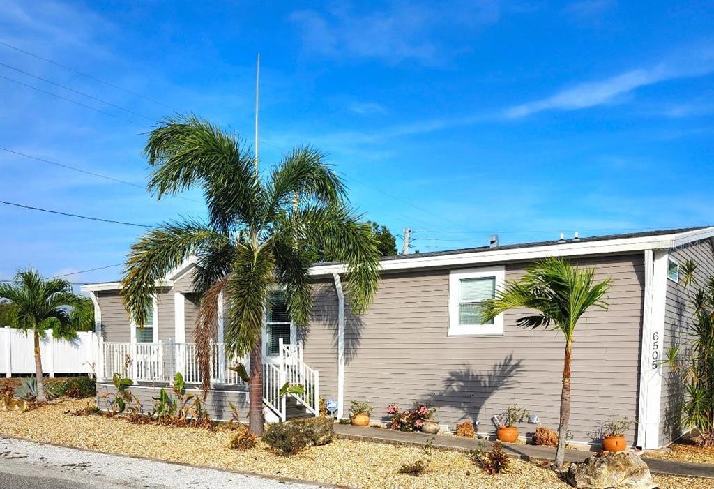 A gray-sided house features a palm tree in the front yard and a white porch — 6505 ARIZONA STREET, BRADENTON, FL