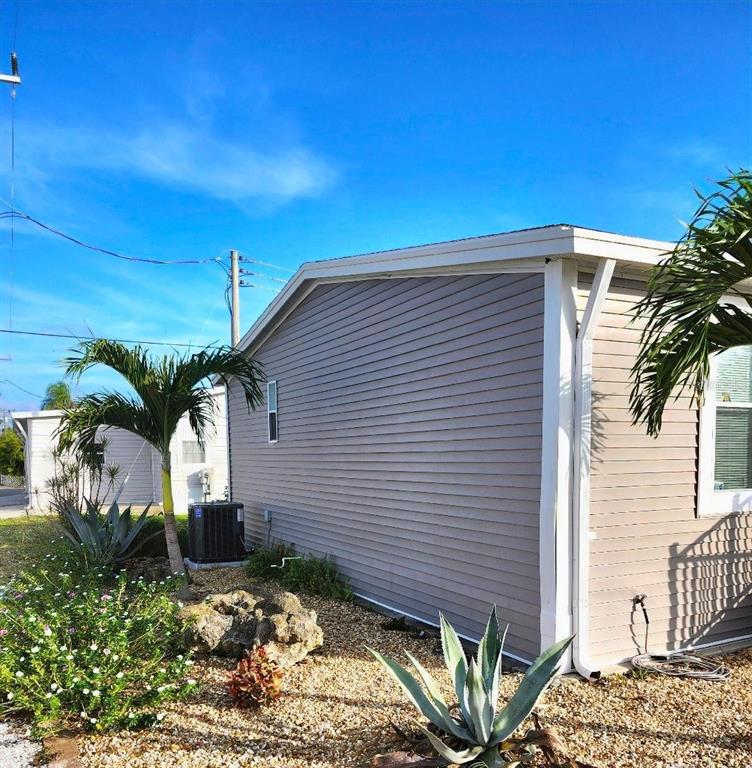 The exterior of a light-colored mobile home features vinyl siding, a small window, and landscaping — 6505 ARIZONA STREET, BRADENTON, FL