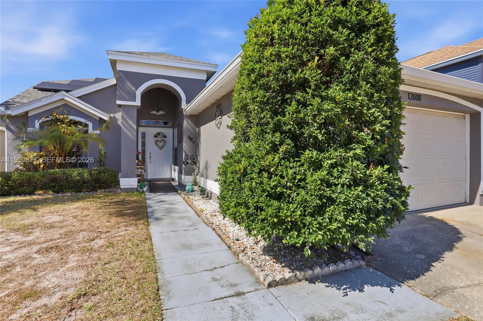 A gray house features a white front door, a large bush, and a garage — 12608 Crayford ave, Orlando FL 32837, ORLANDO, FL