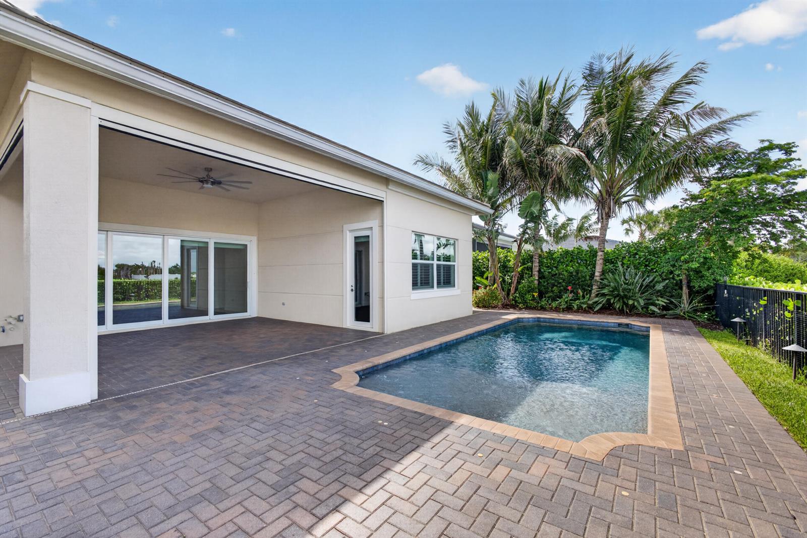A covered patio with brick pavers leads to a rectangular swimming pool in a backyard — 9941 Regency Way, Palm Beach Gardens FL 33412, PALM BEACH GARDENS, FL