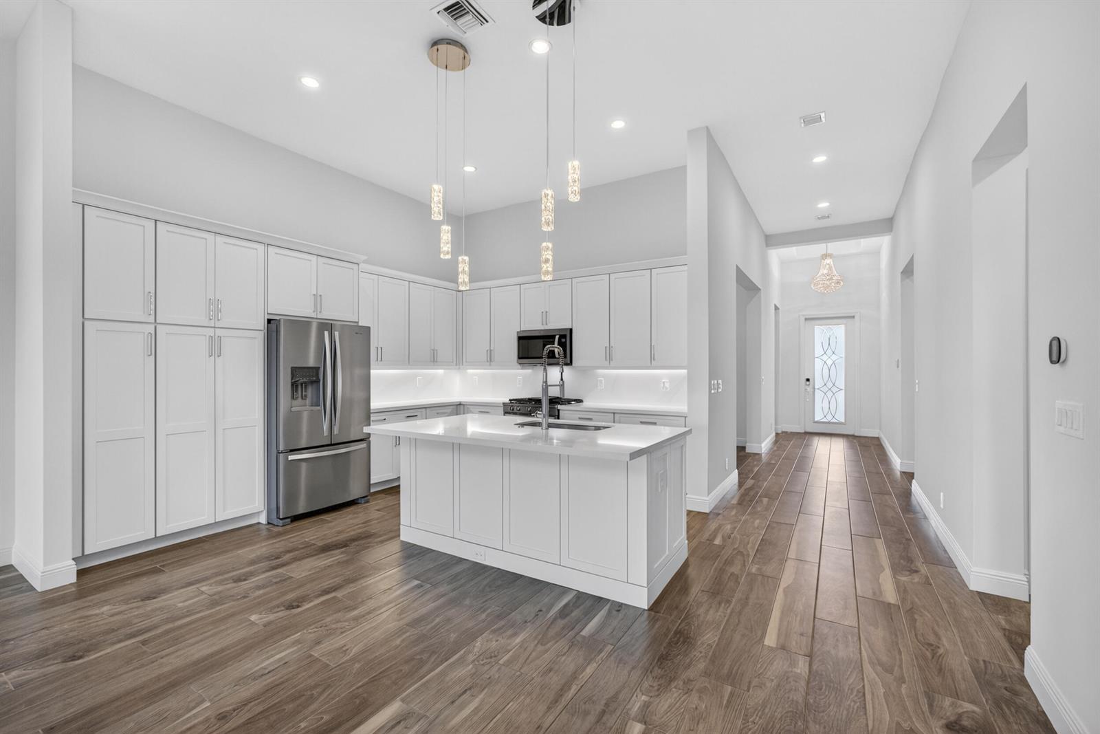 A modern kitchen features white cabinetry, a central island, stainless steel appliances, and wood flooring — 9941 Regency Way, Palm Beach Gardens FL 33412, PALM BEACH GARDENS, FL