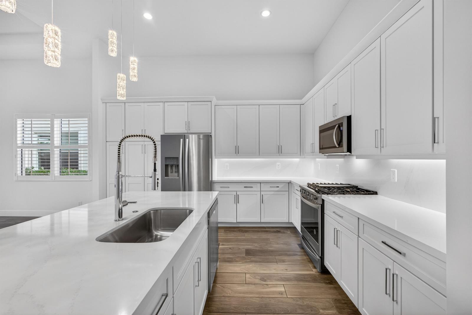A modern kitchen features white cabinetry, stainless steel appliances, a large island, and wood flooring — 9941 Regency Way, Palm Beach Gardens FL 33412, PALM BEACH GARDENS, FL