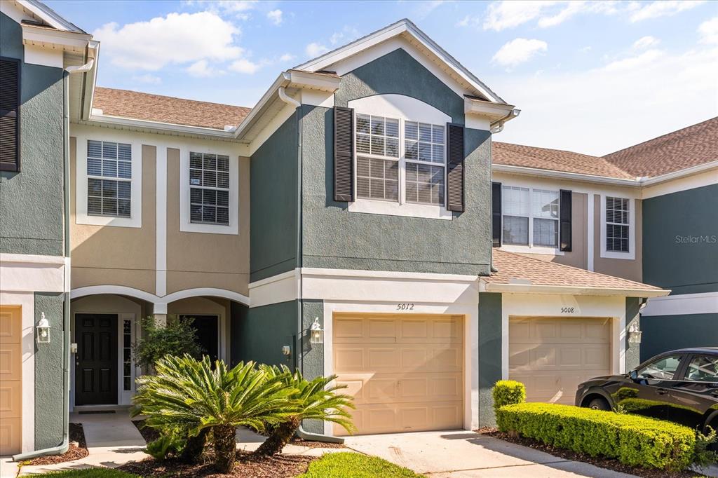 A two-story townhouse exterior features a tan garage, dark shutters, and a small palm tree — 5012 HAWKSTONE DRIVE, SANFORD, FL