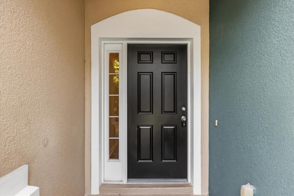 A black front door with a side window light is set within a white frame — 5012 HAWKSTONE DRIVE, SANFORD, FL