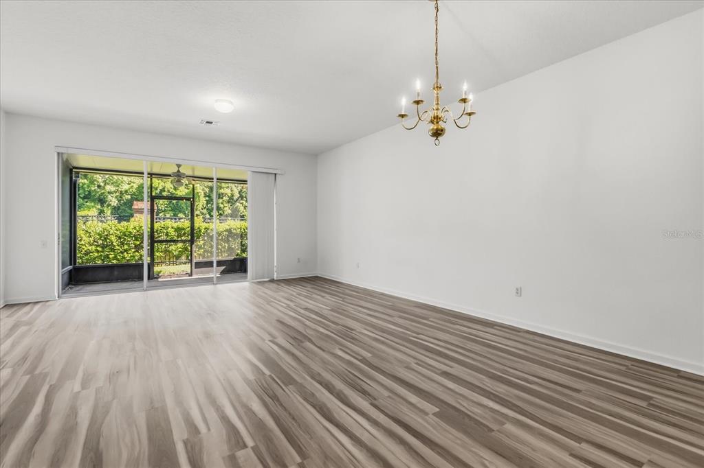 An empty room features light wood-look flooring, white walls, a chandelier, and sliding glass doors — 5012 HAWKSTONE DRIVE, SANFORD, FL