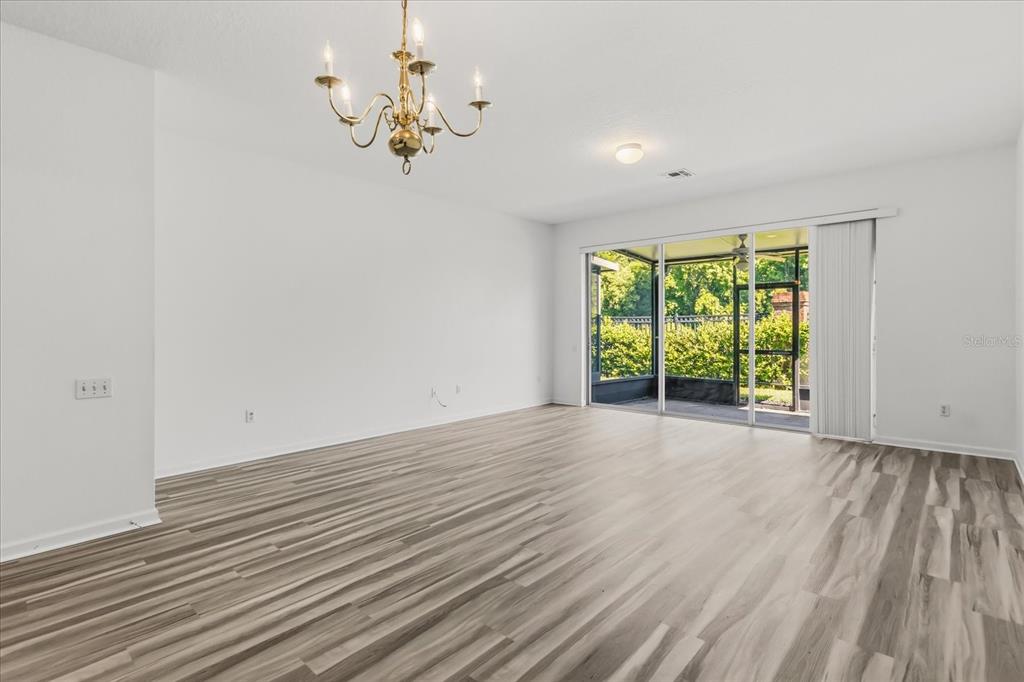 An empty room features light wood-look flooring, a brass chandelier, and sliding glass patio doors — 5012 HAWKSTONE DRIVE, SANFORD, FL