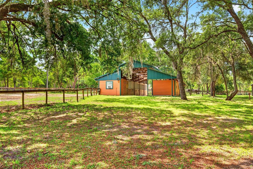 A green and orange barn sits in a grassy, tree-filled pasture with wooden fencing — 11630 SE 78TH STREET, MORRISTON, FL