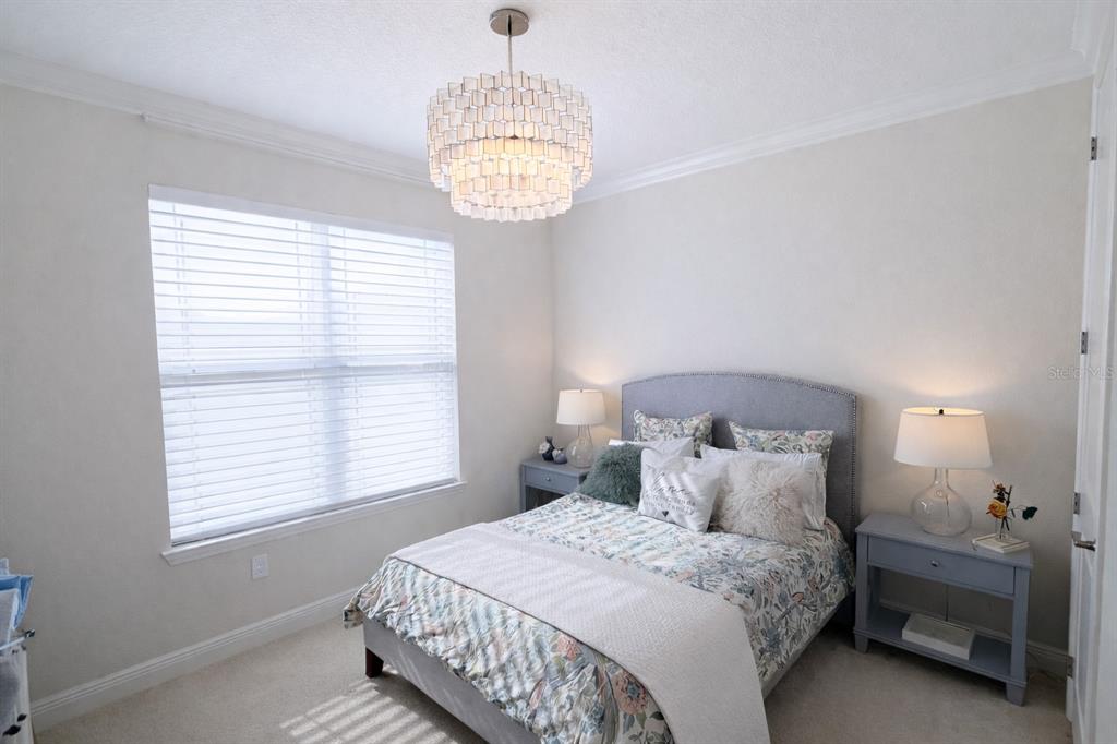 A bedroom features a gray upholstered bed, two matching nightstands, and a tiered glass chandelier — 9241 PATRIMONIO LOOP, WINDERMERE, FL