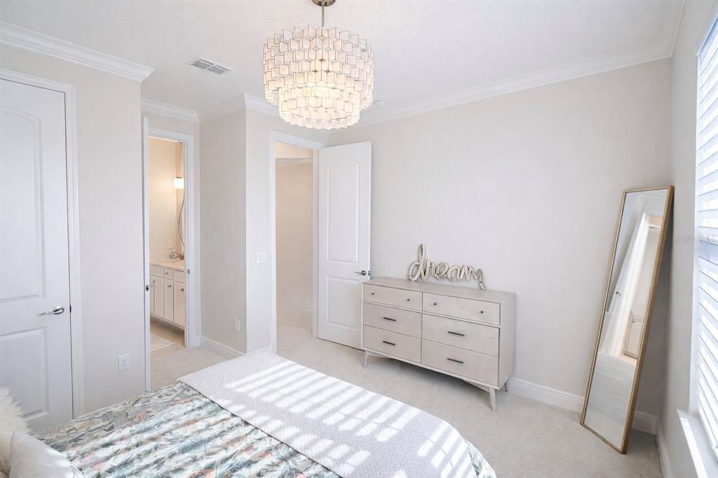 A bedroom features a light-colored dresser, a floor mirror, and a modern tiered chandelier — 9241 PATRIMONIO LOOP, WINDERMERE, FL