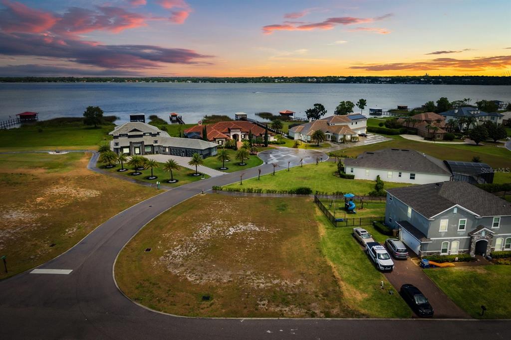 An aerial view shows a vacant residential lot near a lake with several large houses — LOT C-28 SAWGRASS RUN, TAVARES, FL