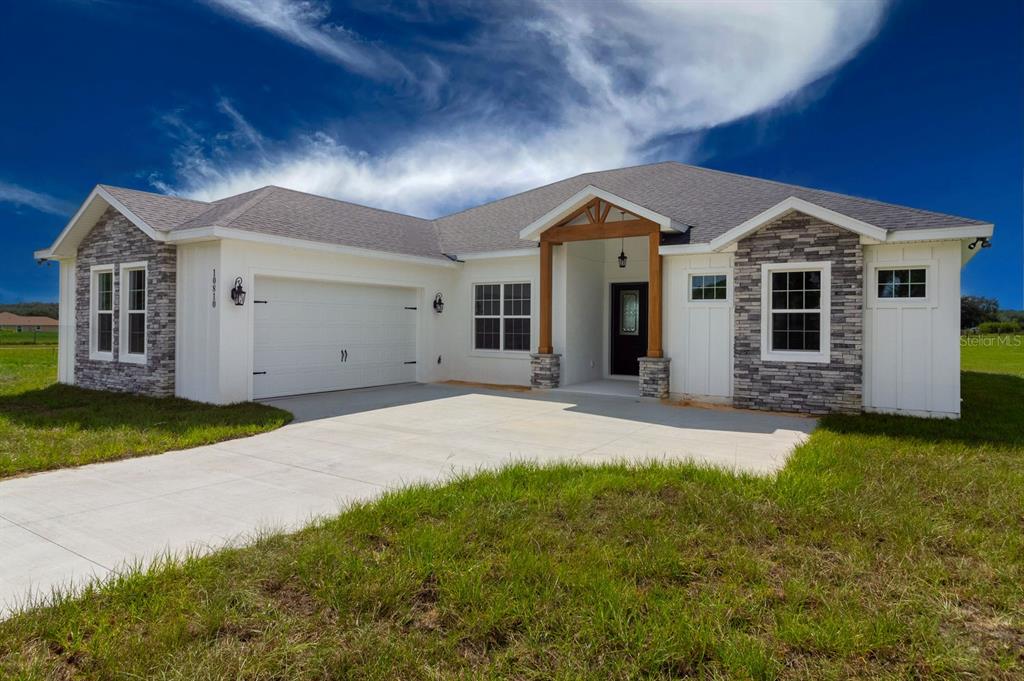 A single-story house with white siding, stone accents, a two-car garage, and a covered entryway — LOT C-28 SAWGRASS RUN, TAVARES, FL