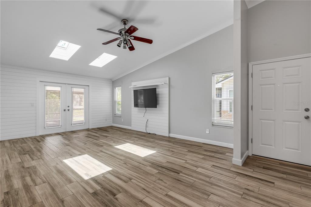 A living room with wood-look tile floors, a vaulted ceiling, skylights, and a wall-mounted television — 240 BOB WHITE COURT UNIT 240, DAYTONA BEACH, FL