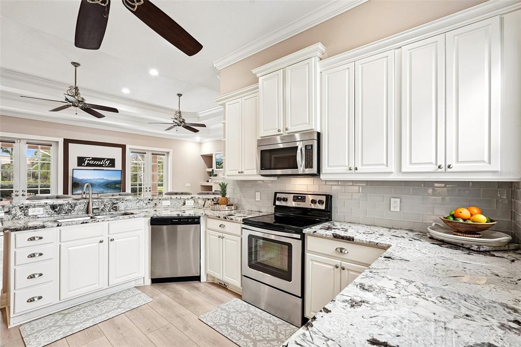 A kitchen features white cabinets, granite countertops, stainless steel appliances, and light wood flooring — 6615 BUTLERS CREST DRIVE, BRADENTON, FL