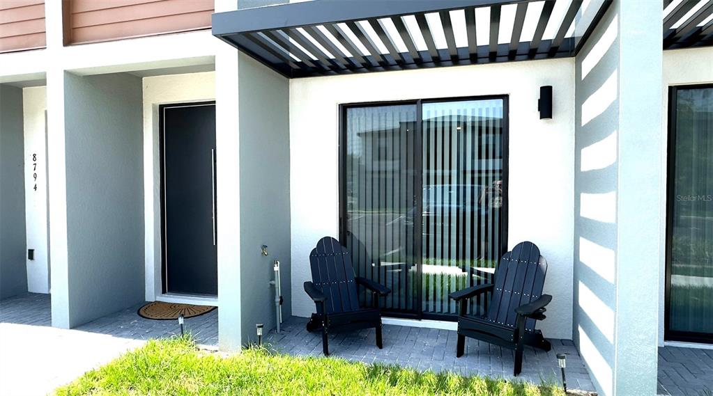 A modern townhouse exterior features a dark front door, sliding glass doors, and two chairs — 8796 POSITIVITY DRIVE, KISSIMMEE, FL