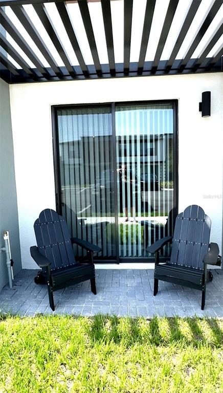 Two black Adirondack chairs sit on a paved patio beneath a pergola outside a sliding door — 8796 POSITIVITY DRIVE, KISSIMMEE, FL