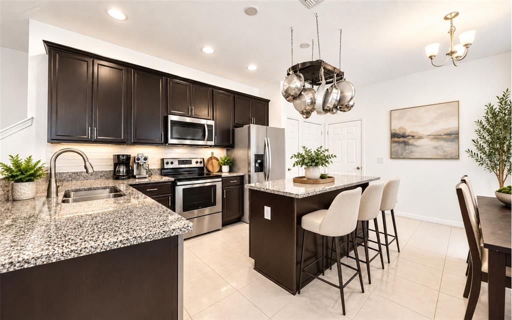 A kitchen features dark wood cabinets, granite countertops, stainless steel appliances, and a hanging pot rack — 1136 E 10TH STREET, APOPKA, FL