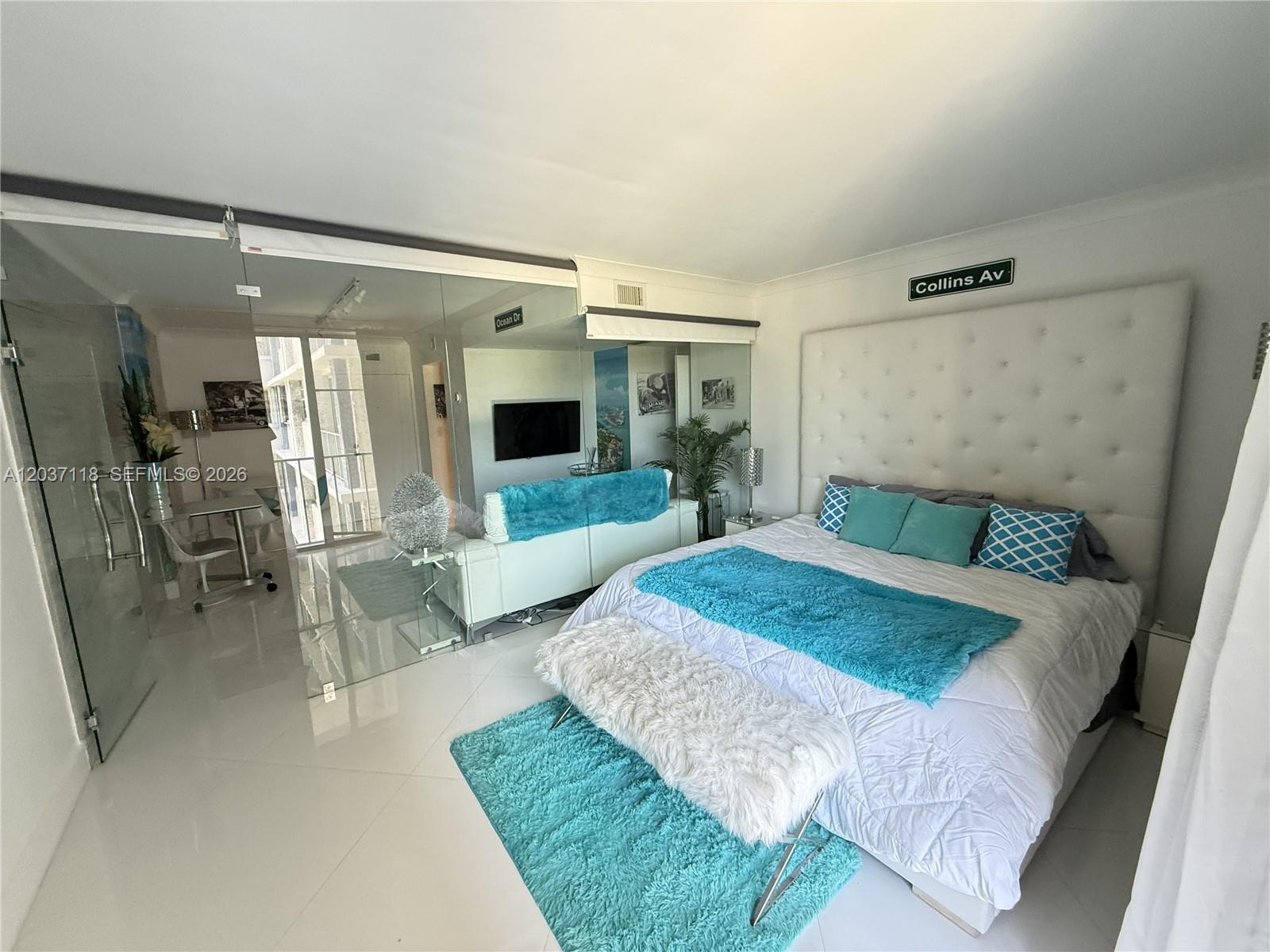 A bedroom features a tufted headboard, white tile floors, and a mirrored wall partition — 800 West Ave # 605, Miami Beach FL 33139, MIAMI BEACH, FL