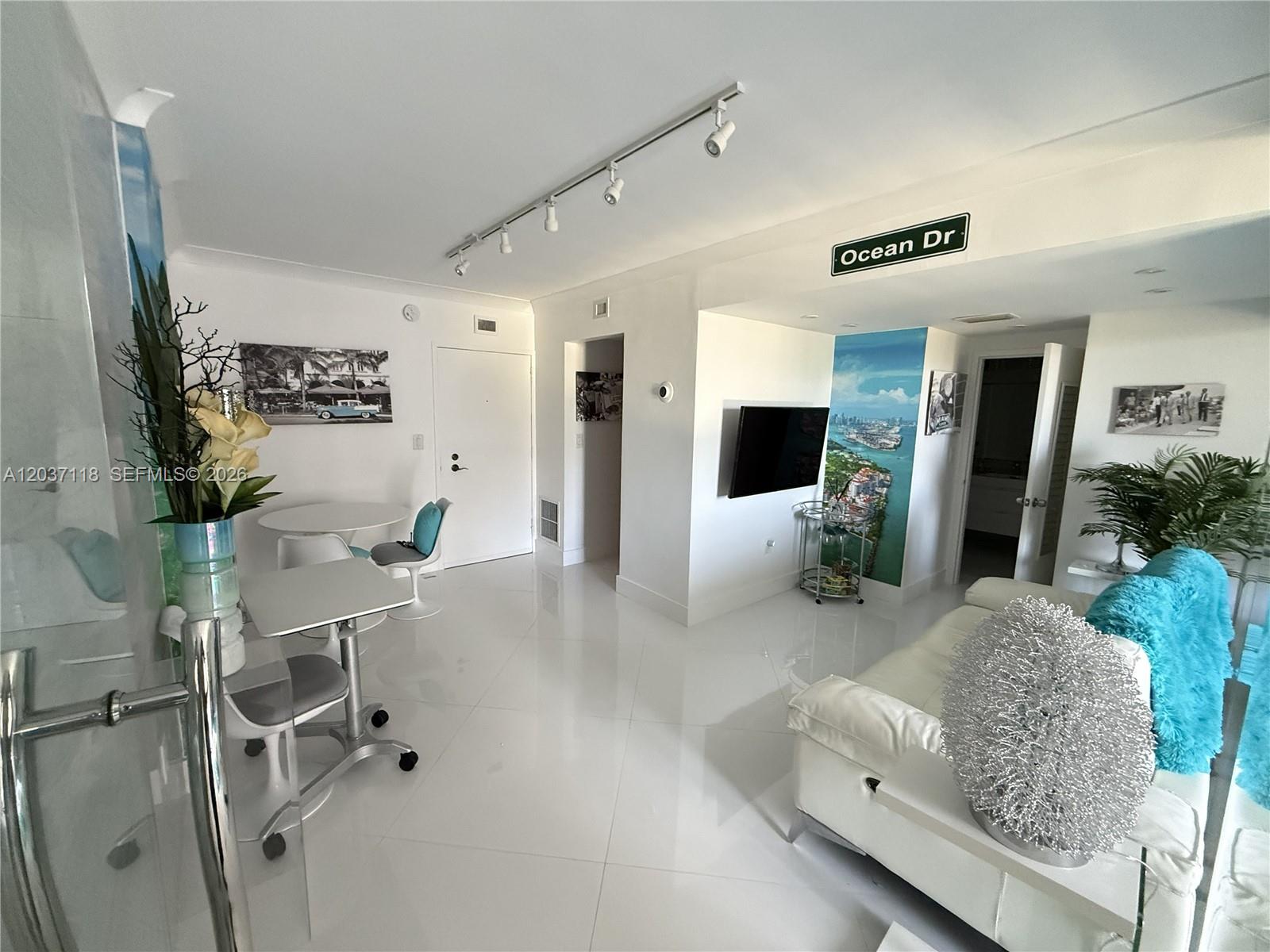 A bright living area features white tile floors, a white sofa, and a wall mural — 800 West Ave # 605, Miami Beach FL 33139, MIAMI BEACH, FL
