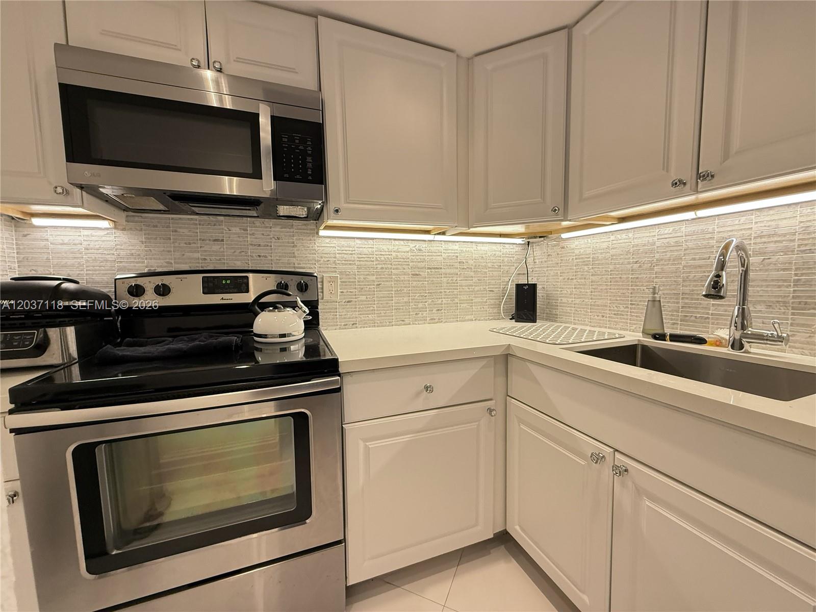 A kitchen features white cabinets, stainless steel appliances, a tiled backsplash, and light countertops — 800 West Ave # 605, Miami Beach FL 33139, MIAMI BEACH, FL