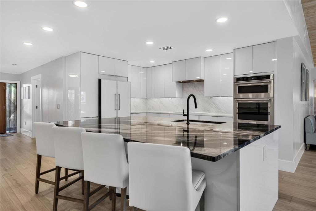 A modern kitchen features white glossy cabinets, a dark marble island, and stainless steel appliances — 8009 13TH AVENUE S, ST PETERSBURG, FL