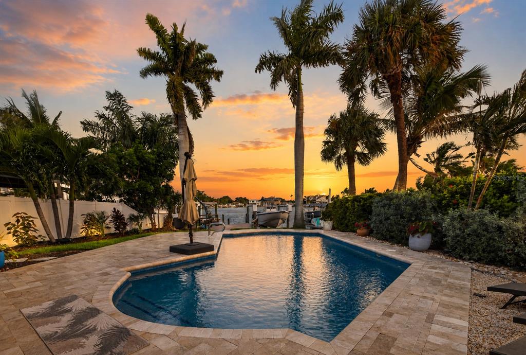 A swimming pool sits on a stone patio surrounded by palm trees at sunset — 8009 13TH AVENUE S, ST PETERSBURG, FL