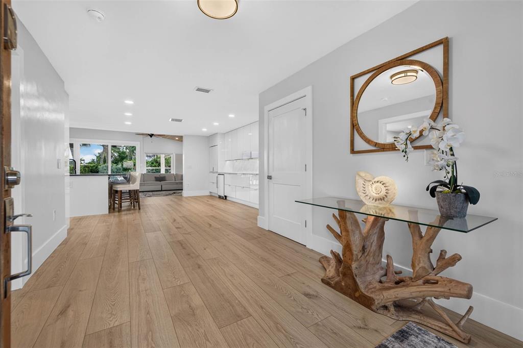 A bright entryway features light wood flooring, a glass-topped driftwood console table, and white cabinetry — 8009 13TH AVENUE S, ST PETERSBURG, FL
