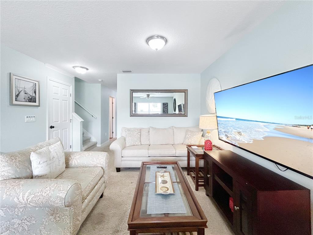 A living room features a beige sofa, a patterned loveseat, and a large wall-mounted television — 2749 CLUB CORTILE CIRCLE, KISSIMMEE, FL