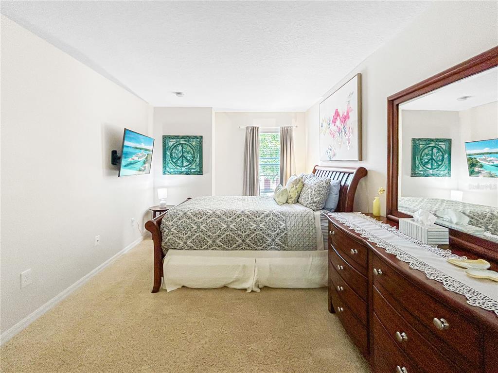 A bedroom features a bed, a wooden dresser with a mirror, and a wall-mounted television — 2749 CLUB CORTILE CIRCLE, KISSIMMEE, FL
