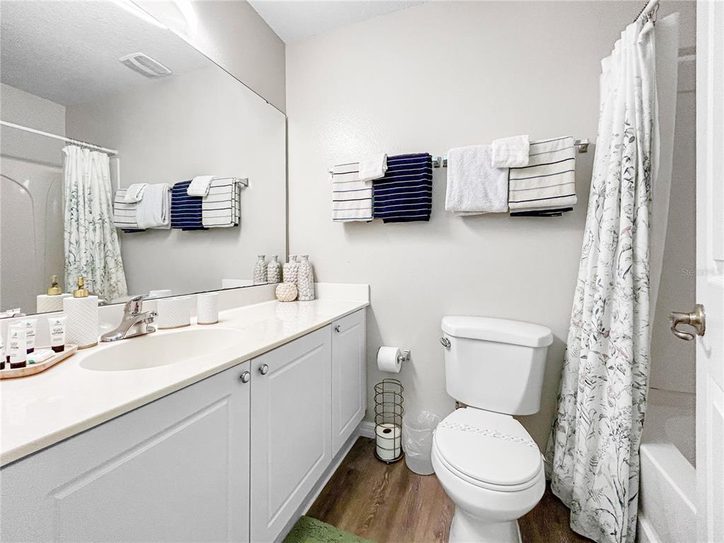 A bathroom features a white vanity, a toilet, and a shower with a floral curtain — 2749 CLUB CORTILE CIRCLE, KISSIMMEE, FL