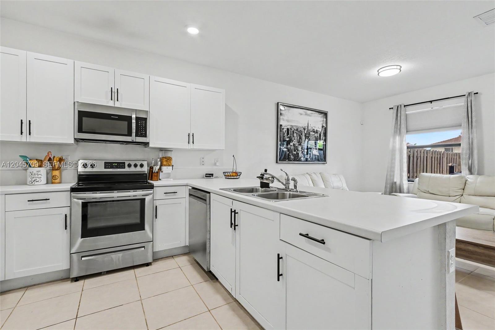 A modern kitchen features white cabinetry, stainless steel appliances, and a central island with sink — 18102 SW 148th Rd, Miami FL 33187, MIAMI, FL