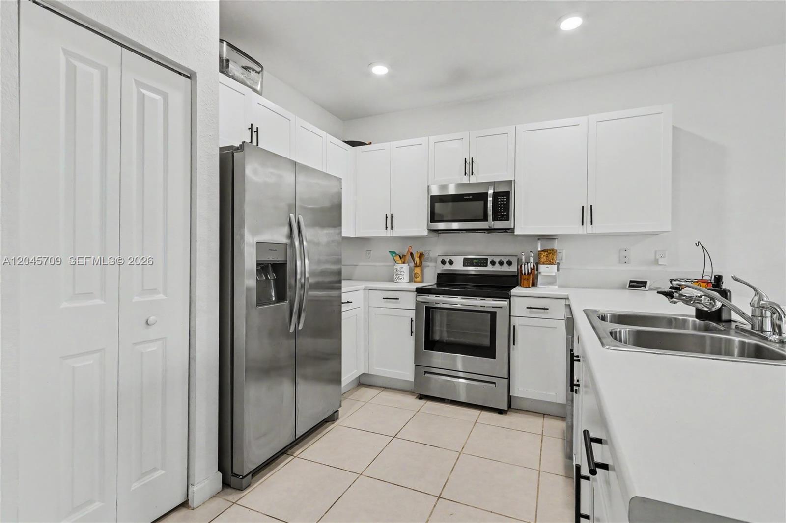 A kitchen features white cabinets, stainless steel appliances, and light-colored tile flooring — 18102 SW 148th Rd, Miami FL 33187, MIAMI, FL