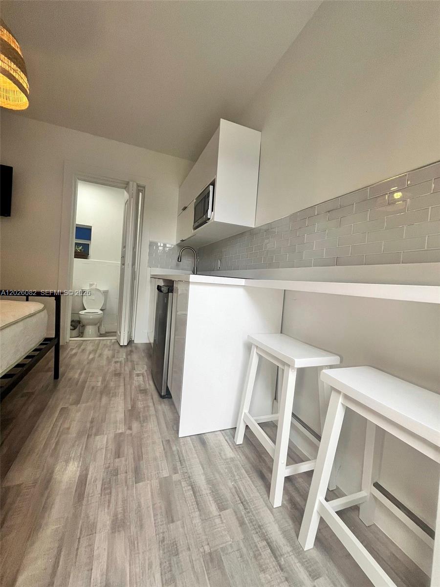 A small kitchen area features white cabinets, a subway tile backsplash, and two bar stools — 1845 NW 114th St # 0, Miami FL 33167, MIAMI, FL