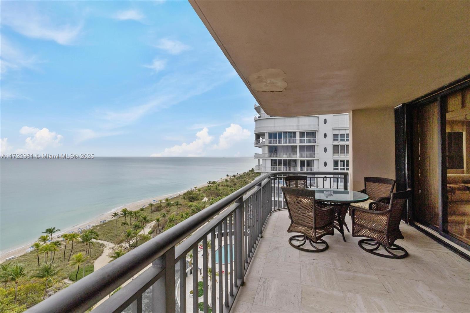 A balcony with wicker furniture overlooks a sandy beach and the ocean — 10175 Collins Ave # 1202, Bal Harbour FL 33154, BAL HARBOUR, FL