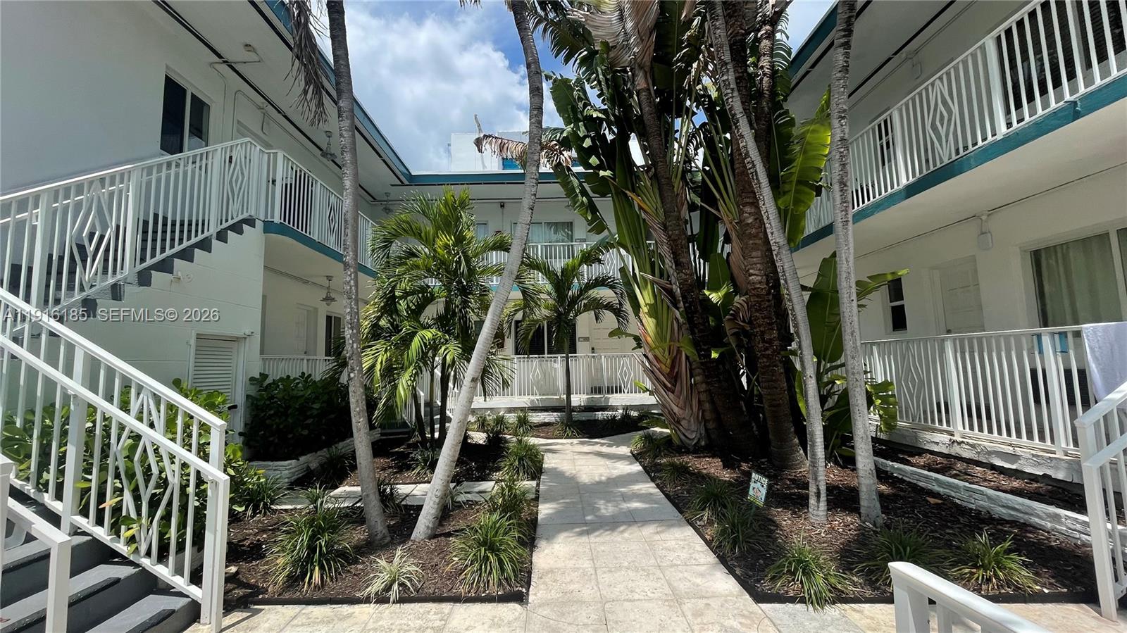 A courtyard with a stone walkway, tropical plants, and white balconies at a multi-story building — 7710 Harding Ave # 408, Miami Beach FL 33141, MIAMI BEACH, FL