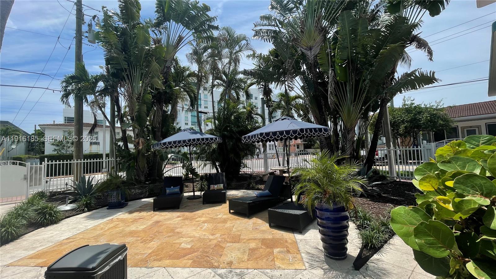 A patio area features lounge chairs, umbrellas, and potted plants on a stone-tiled surface — 7710 Harding Ave # 408, Miami Beach FL 33141, MIAMI BEACH, FL