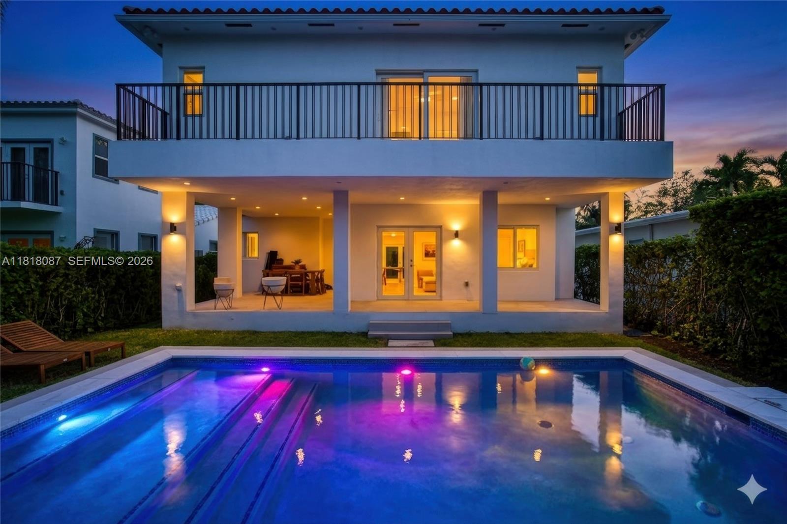 A two-story house with a covered patio, balcony, and illuminated swimming pool at dusk — 719 W 51st St, Miami Beach FL 33140, MIAMI BEACH, FL