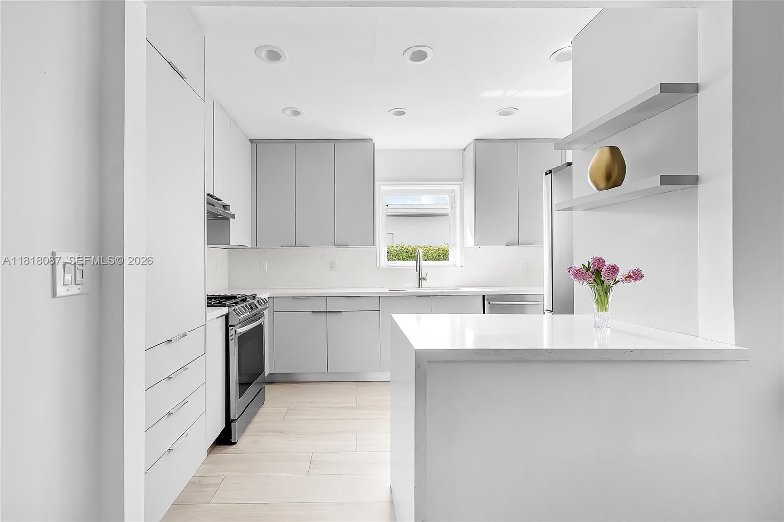 A modern kitchen features light gray cabinets, white countertops, stainless steel appliances, and open shelving — 719 W 51st St, Miami Beach FL 33140, MIAMI BEACH, FL