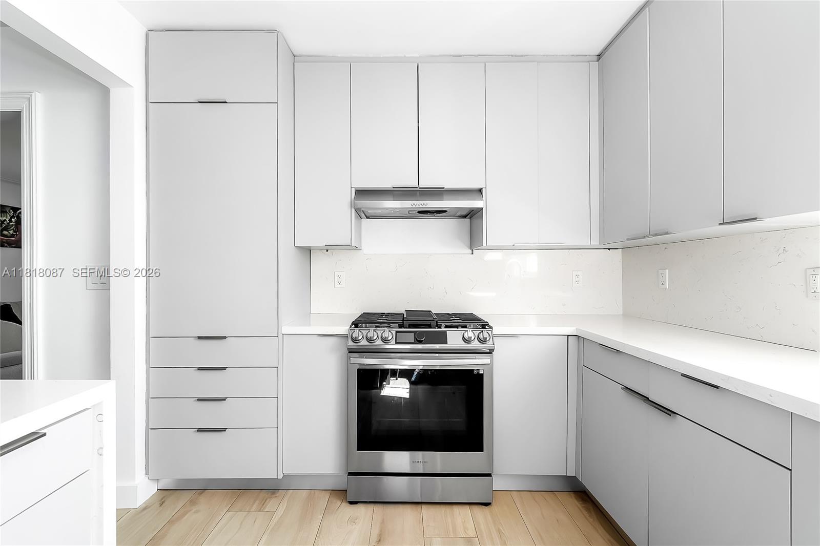 A modern kitchen features light gray flat-panel cabinetry, stainless steel appliances, and white countertops — 719 W 51st St, Miami Beach FL 33140, MIAMI BEACH, FL