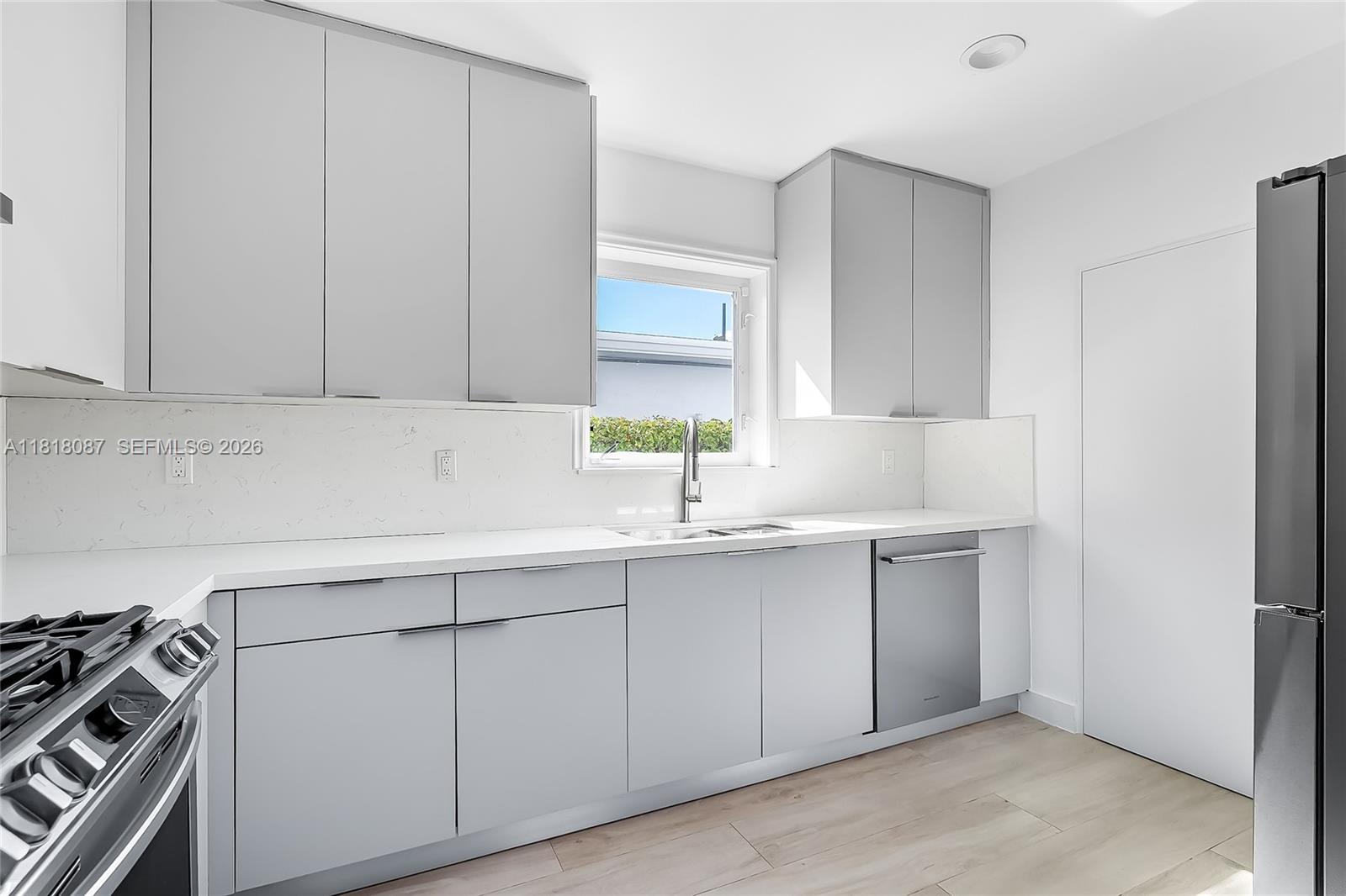 A modern kitchen features light gray cabinets, white countertops, and stainless steel appliances — 719 W 51st St, Miami Beach FL 33140, MIAMI BEACH, FL