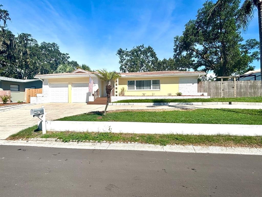 A single-story house with a two-car garage, yellow siding, and a front lawn — 1201 KAPOK KOVE CIRCLE, CLEARWATER, FL