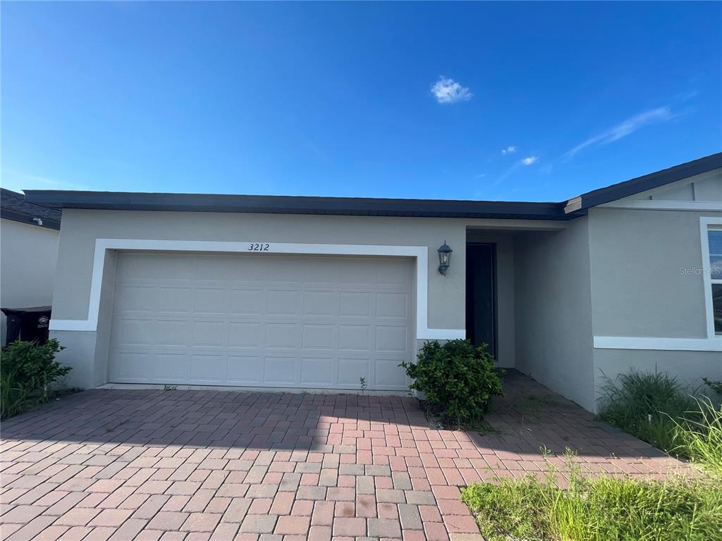 A single-story house exterior features a two-car garage, a paved driveway, and a recessed entryway — 3212 WEITZEL DRIVE, HAINES CITY, FL