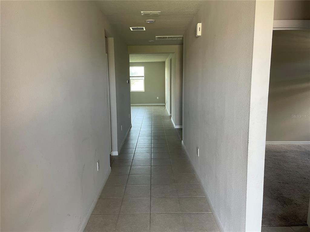 A long hallway with light-colored tile flooring leads toward a window in the distance — 3212 WEITZEL DRIVE, HAINES CITY, FL