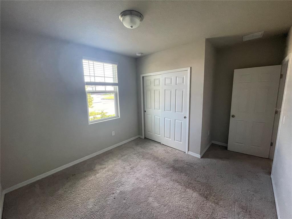 An empty bedroom features beige carpet, light gray walls, a window, and two white doors — 3212 WEITZEL DRIVE, HAINES CITY, FL