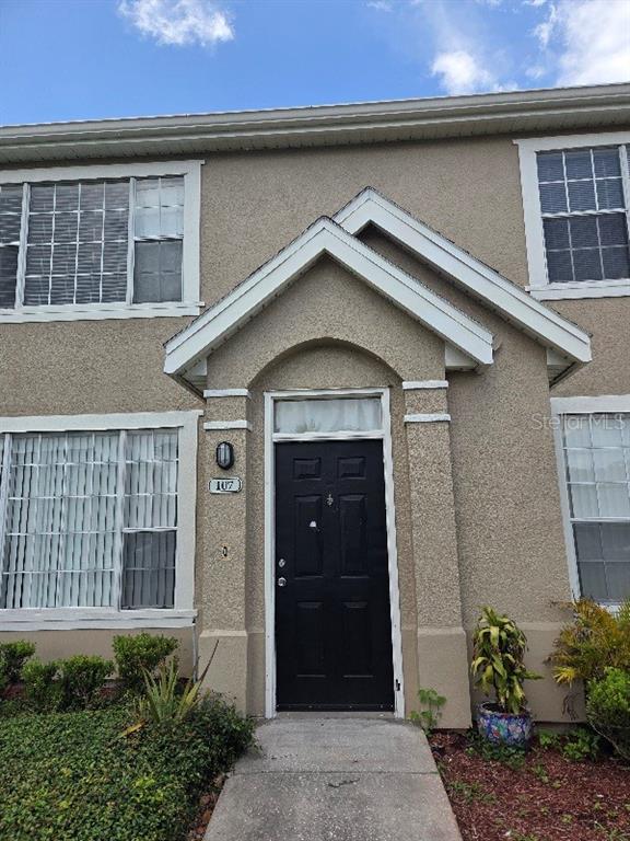 The exterior of a two-story tan stucco townhouse features a black front door and windows — 9165 LEE VISTA BOULEVARD UNIT 107, ORLANDO, FL