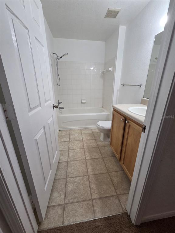 A bathroom features a white tub-shower combination, a wood vanity, and beige tile flooring — 9165 LEE VISTA BOULEVARD UNIT 107, ORLANDO, FL