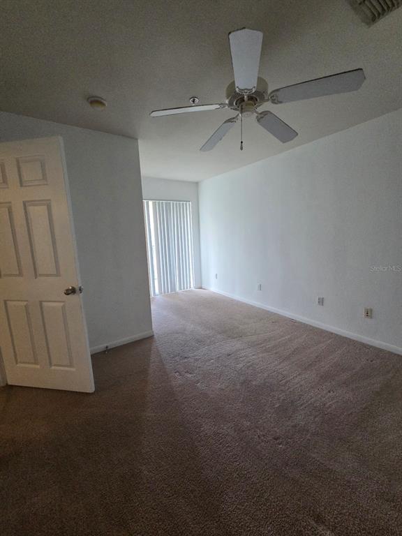 An empty bedroom features beige carpeting, white walls, a ceiling fan, and sliding glass doors — 9165 LEE VISTA BOULEVARD UNIT 107, ORLANDO, FL